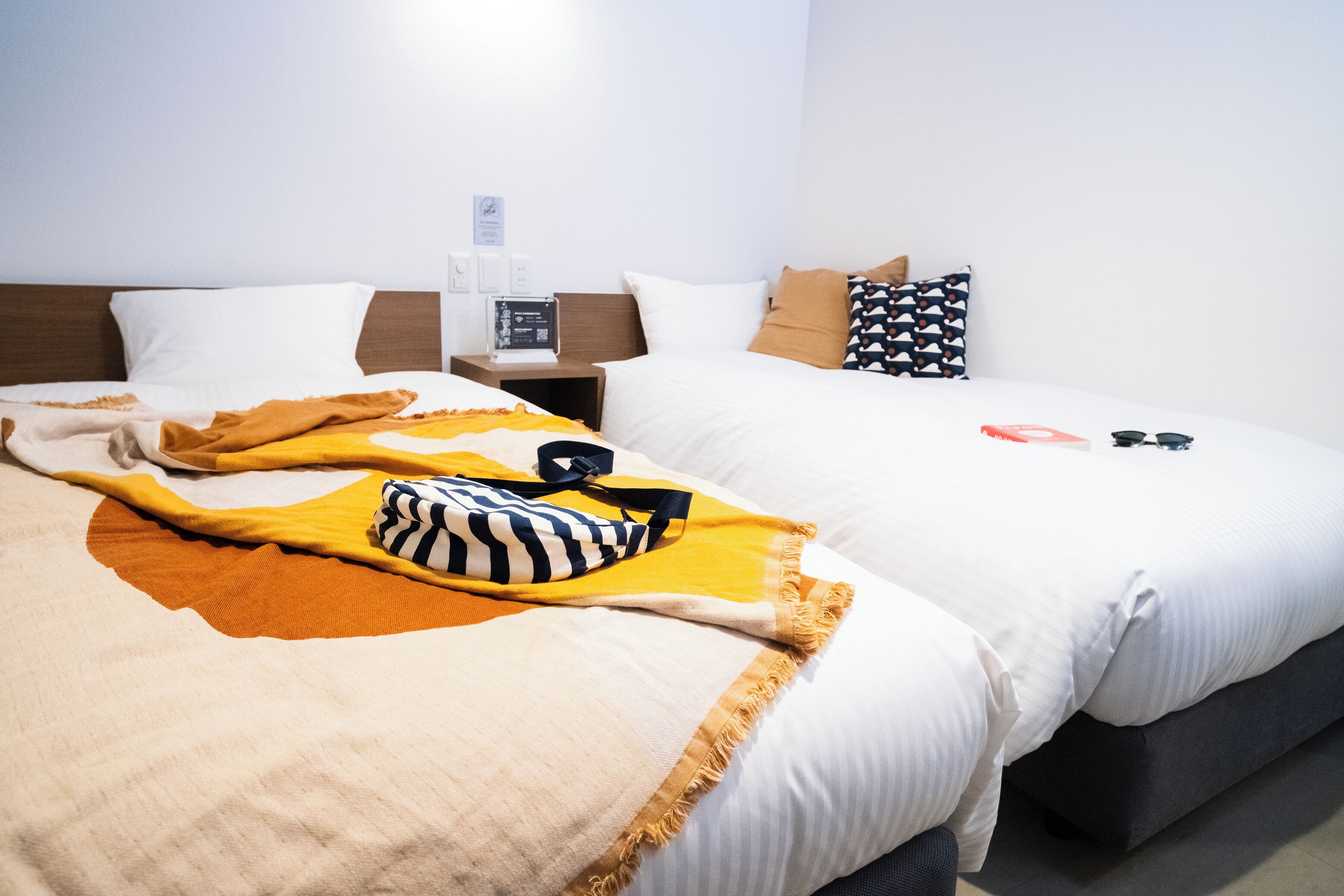 A hotel room with two beds, a nightstand with a radio, and a wall-mounted thermostat.