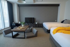 A modern hotel room with a bed, a TV, a dining table with chairs, and a sofa.