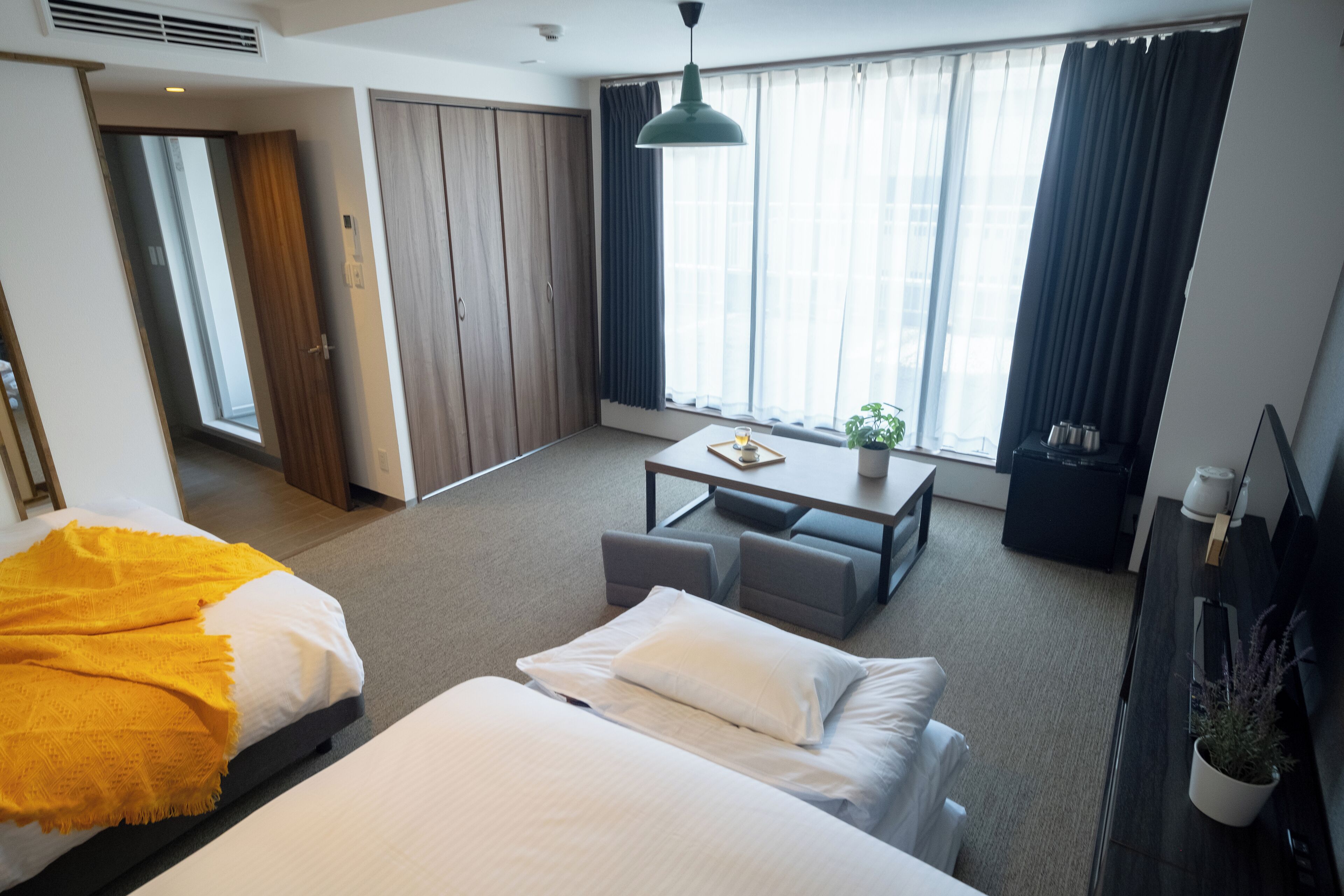 Een hotelkamer met een bed, een bureau, een stoel, een bank, een kamerplant en een kledingkast.