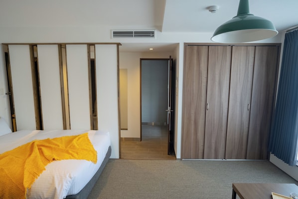 A hotel room with a bed, a wardrobe, a desk, and a hanging light fixture.
