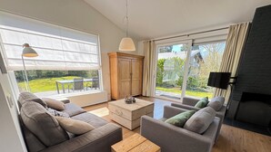 Un salon moderne avec des canapés gris, une table basse en bois et une vue sur un jardin grâce à de grandes fenêtres.