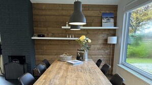Une salle à manger moderne avec une table en bois, des chaises noires, un luminaire suspendu et une vue sur l’extérieur grâce à une grande fenêtre.