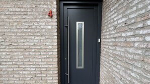 Une porte noire avec une poignée verticale et une petite fenêtre rectangulaire.