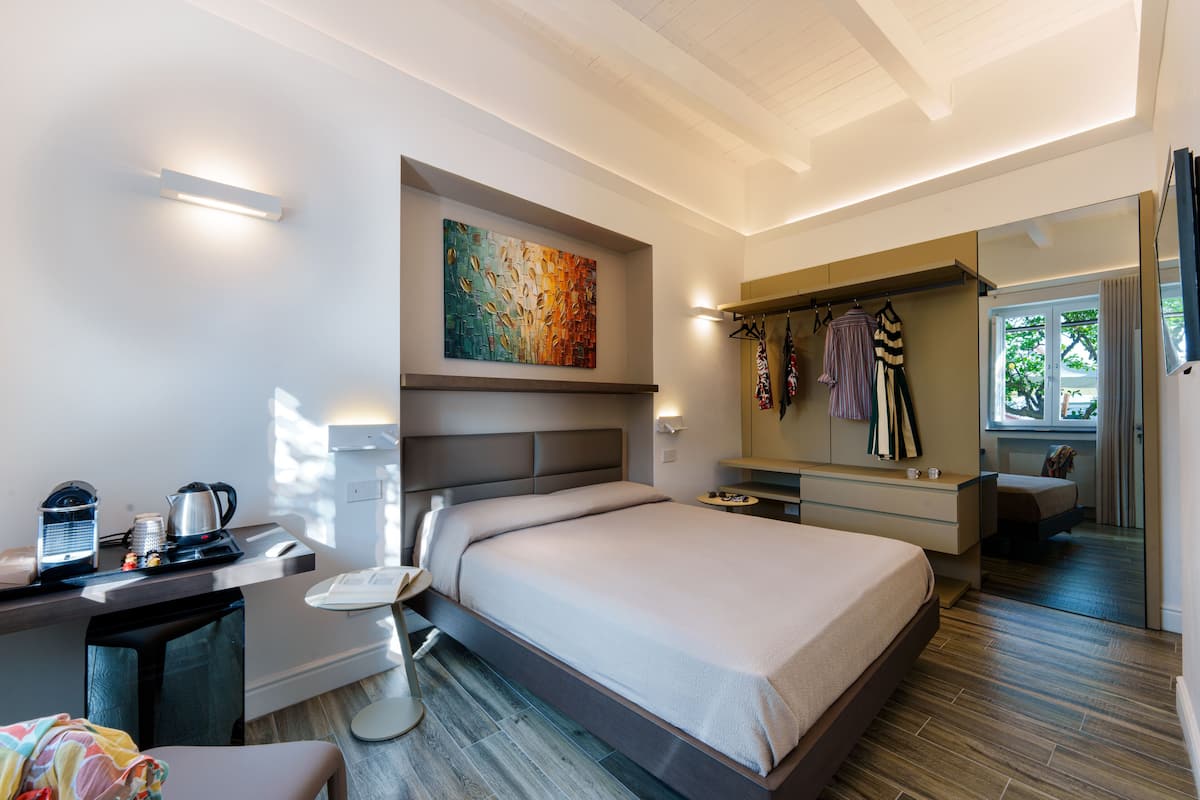 Una habitación de hotel moderna con una cama grande, un escritorio con un hervidor, una silla y un cuadro en la pared.