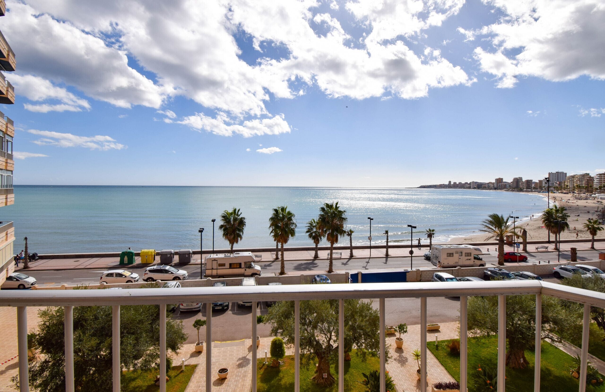 A balcony with a view of a beach, palm trees, and a clear sky.