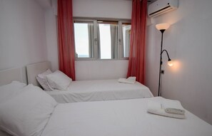 Habitación de hotel con dos camas, una ventana con cortinas, un equipo de aire acondicionado y una lámpara de noche.