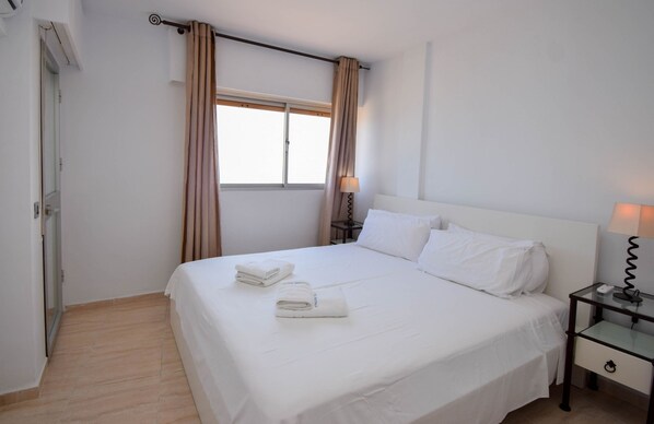 A hotel room with a bed, a bedside table with a lamp, a window with curtains, and a door. - Ref 318 Sea front 2 bedroom apartment in the centre of Fuengirola next to the port (Fuengirola)