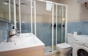 Une salle de bain avec une douche à parois de verre, un lavabo blanc, des toilettes et un lave-linge.