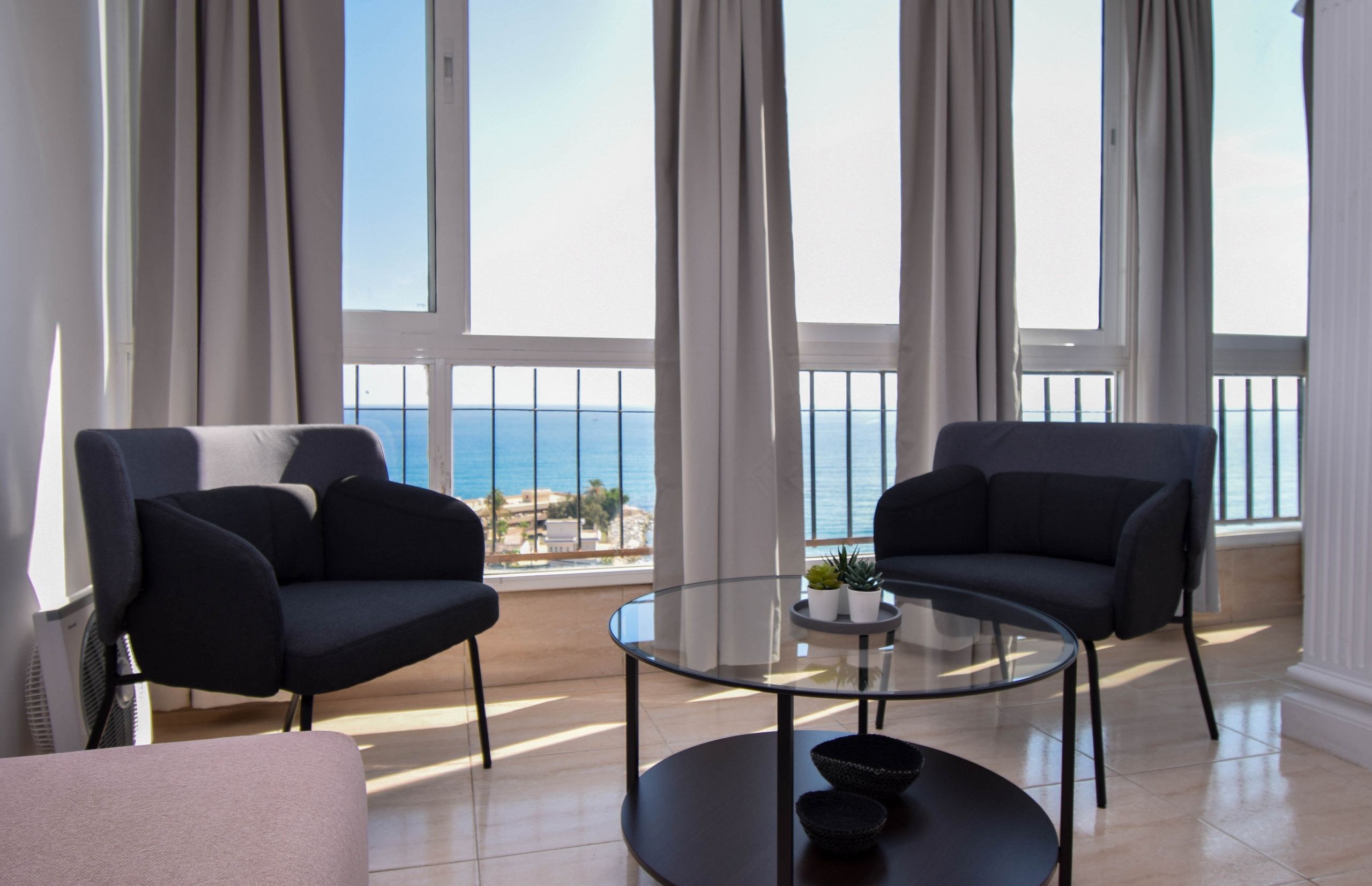 A modern living room with two sofas, a glass coffee table, and a view of the sea.