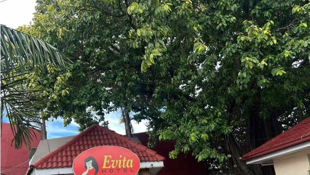 A hotel named Evita with a red sign, surrounded by lush greenery and a tiled walkway. - OYO 1026 Evita Hotel Bacoor (Bacoor City)