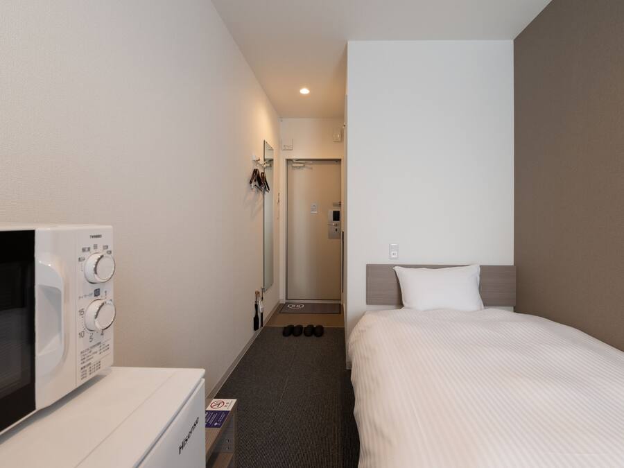 A hotel room with a bed, a microwave, and a small kitchenette.