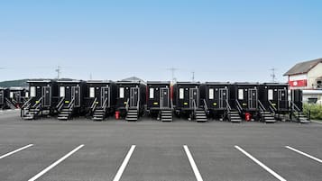 Una hilera de baños portátiles negros con números en las puertas, ubicados en un estacionamiento con líneas blancas en el suelo.