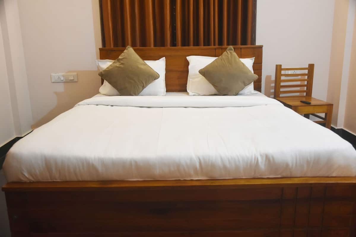 Un lit bien fait, avec des draps blancs et deux oreillers, une tête de lit en bois et une petite table de chevet en bois sur laquelle se trouve une télécommande.