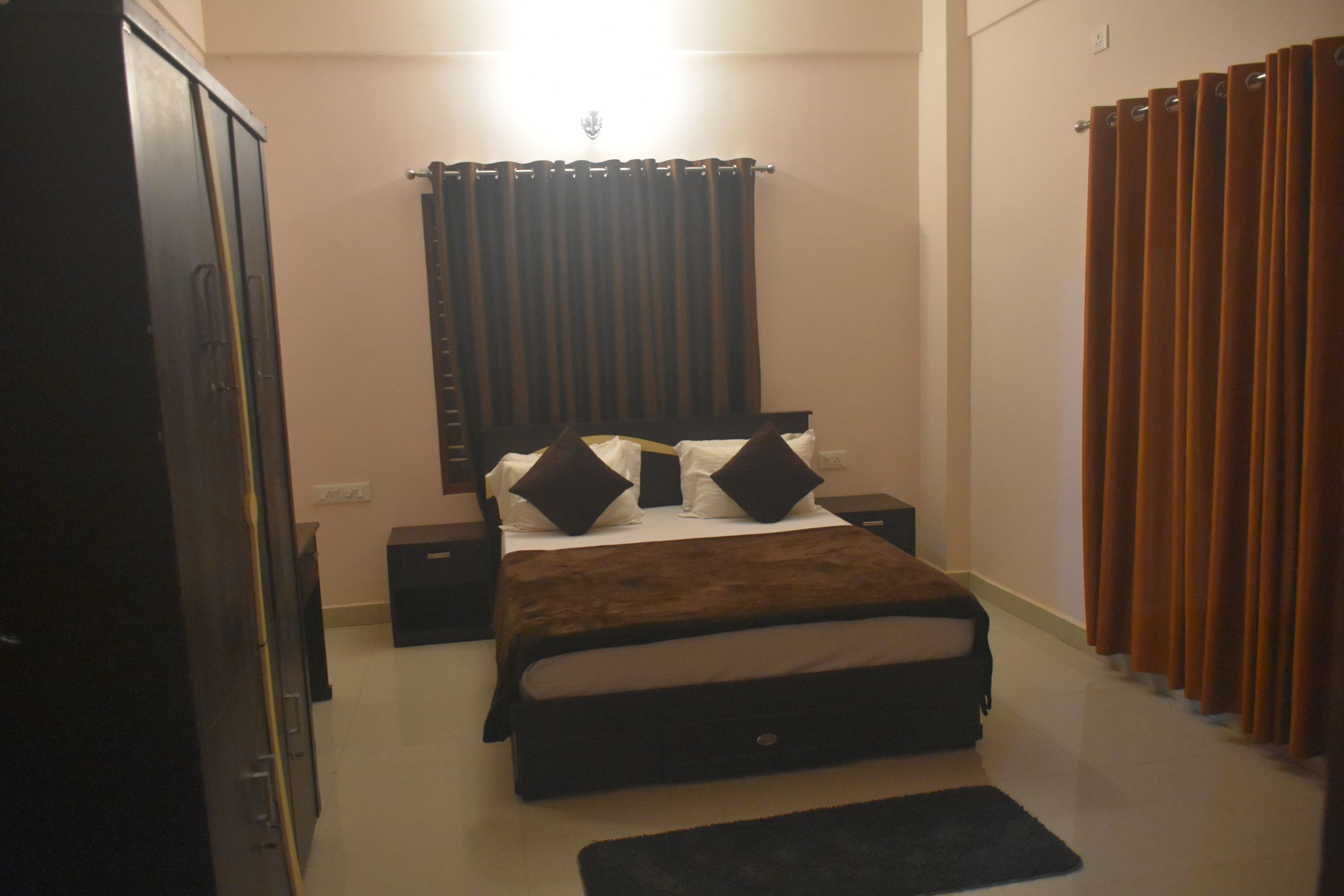 Quarto com cama, mesas de cabeceira, guarda-roupa e cortinas.