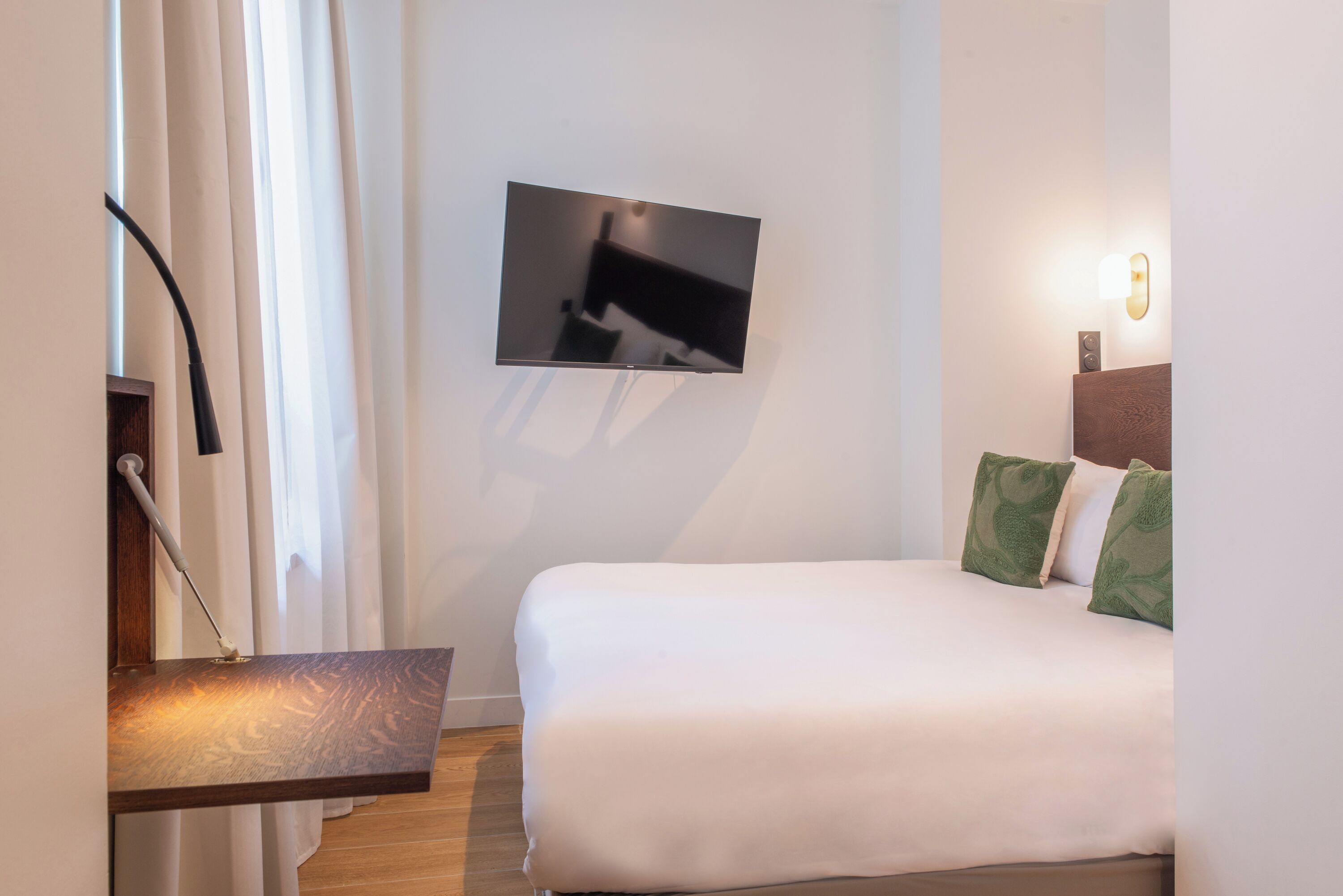 Ein Hotelzimmer mit Bett, einem Wand-Fernseher, einem Nachttisch und einer Wandleuchte.