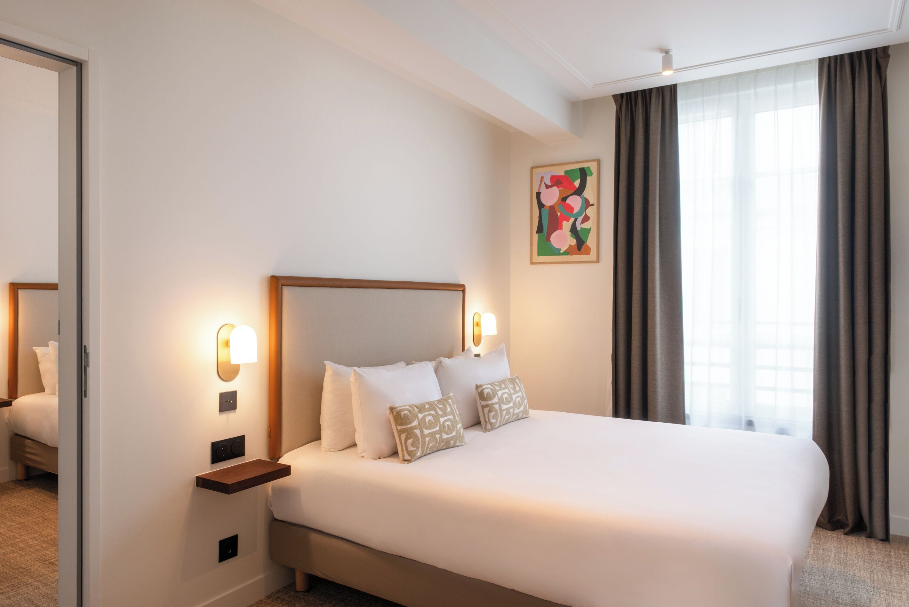 Habitación de hotel con una cama grande, mesitas de noche, un espejo y un cuadro en la pared.