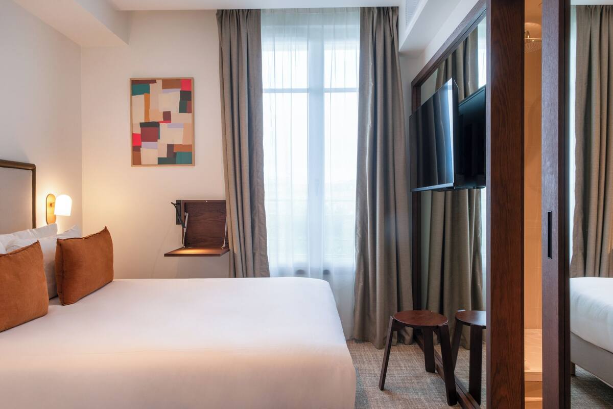 Une chambre d’hôtel avec un grand lit, un téléviseur fixé au mur, une petite table et une chaise.