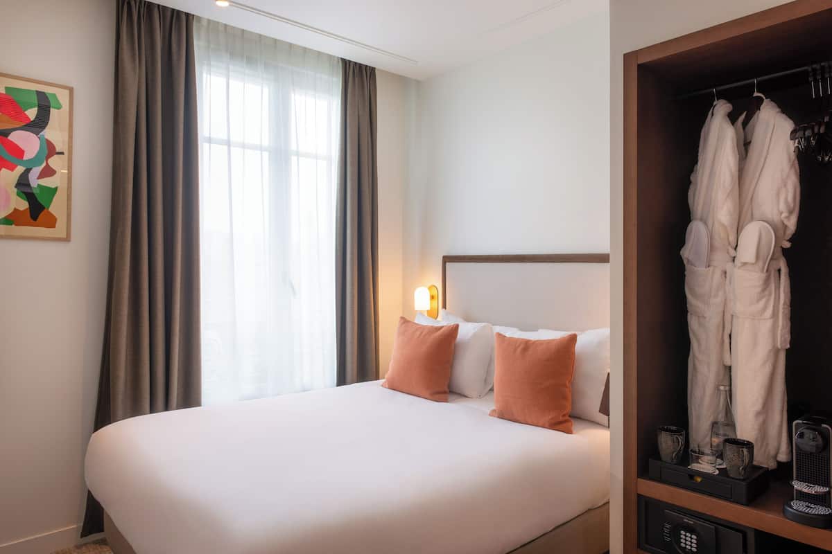 Une chambre d’hôtel avec un grand lit, une table de chevet avec une lampe, un peignoir suspendu à un porte-manteau et un tableau accroché au mur.