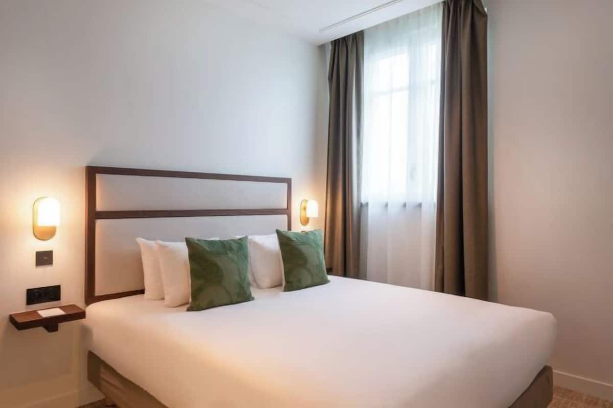 Une chambre d’hôtel avec un lit, deux lampes de chevet, une table de chevet et une fenêtre avec des rideaux.