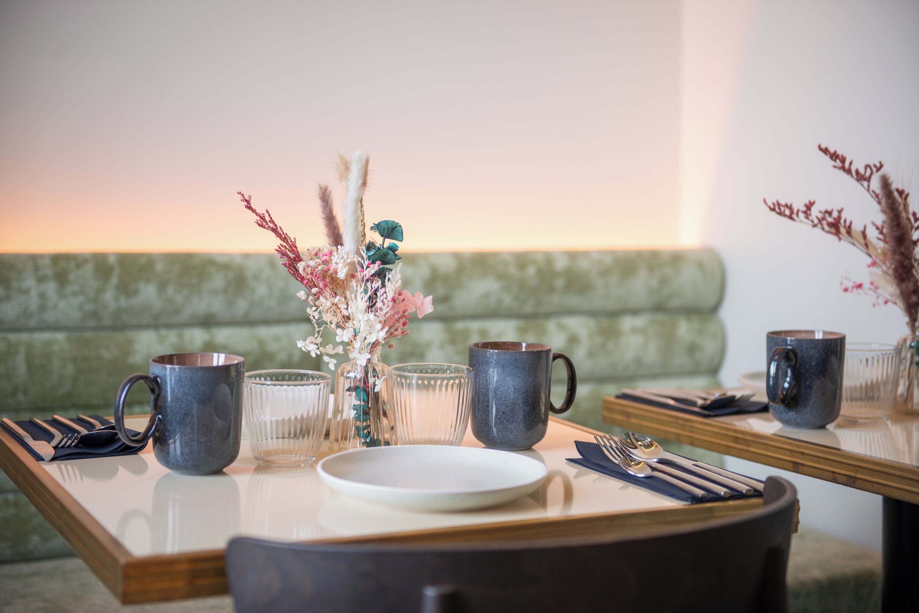 Una mesa de comedor dispuesta con un florero, dos tazas, un plato y cubiertos.