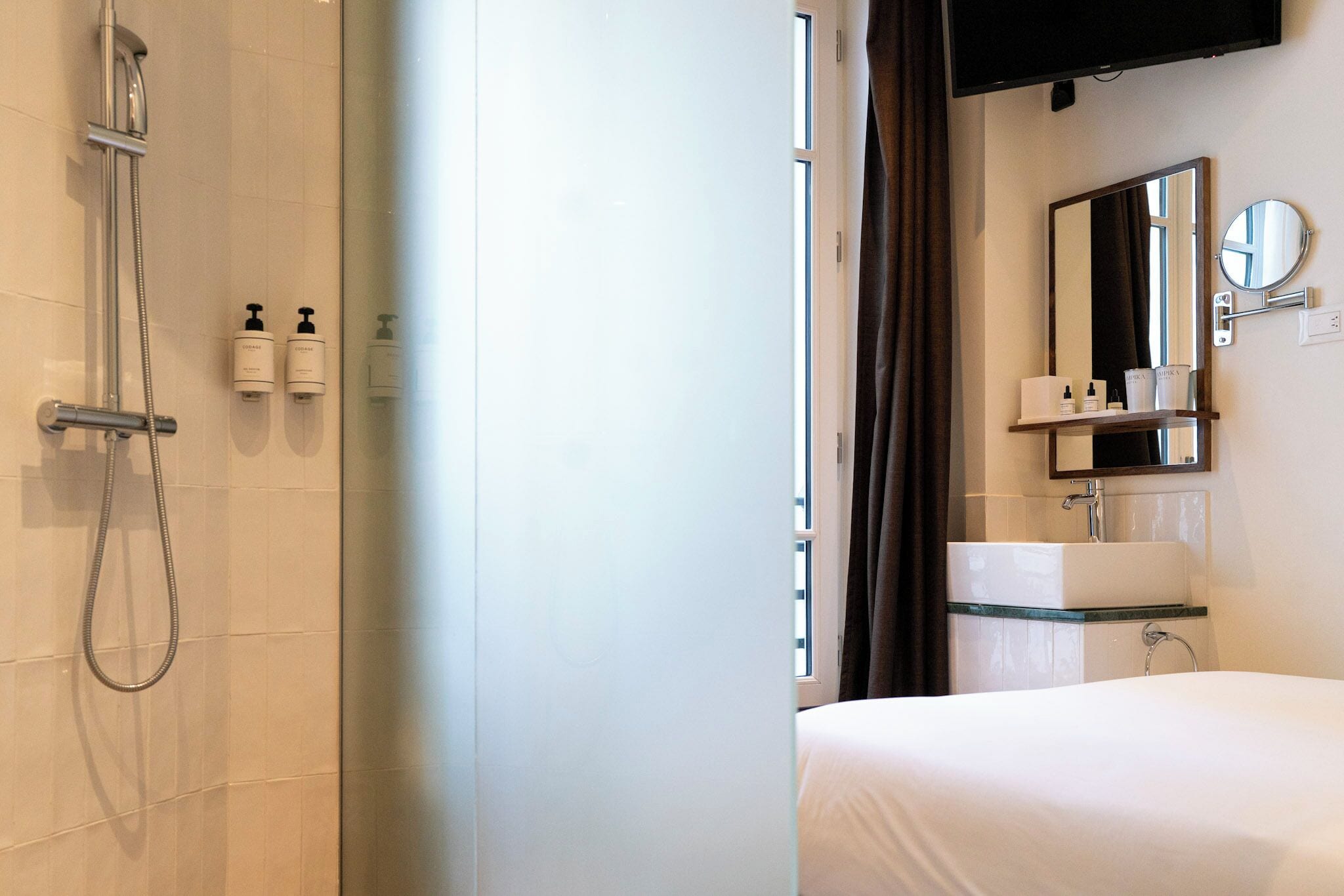 A hotel bathroom with a shower, a sink, a mirror, and toiletries on the wall.