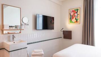 A hotel room with a bed, a TV mounted on the wall, a sink with a mirror, and a towel rack.