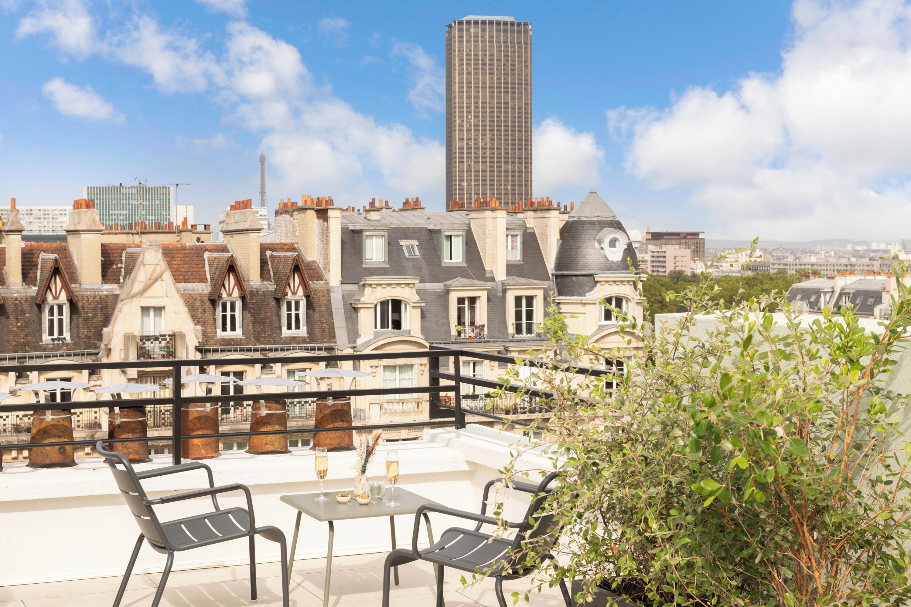 A rooftop terrace with a table and chairs, overlooking a cityscape with historic buildings and a tall skyscraper.