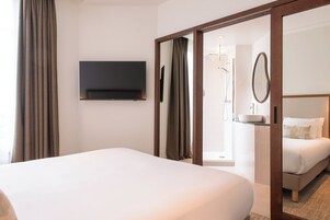 Ett hotellrum med en säng, en tv som är monterad på väggen, ett badrum med dusch och en spegel på väggen.