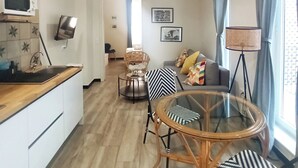 Une cuisine moderne équipée d’un four à micro-ondes, d’un évier et d’un plan de travail en bois. On y trouve un coin repas avec une table et des chaises en verre, ainsi qu’un canapé agrémenté de coussins à motifs. La pièce est dotée d’un parquet et d’un plafond avec des lambris.