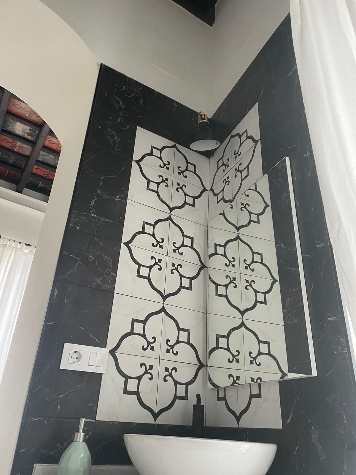 Un baño con pared de azulejos blanco y negro, un lavabo blanco y un espejo.