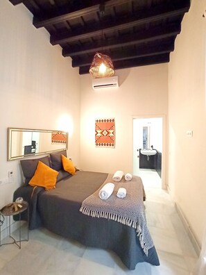 Een slaapkamer met een bed, nachtkastje, spiegel, wandairconditioner en een deur naar een badkamer.