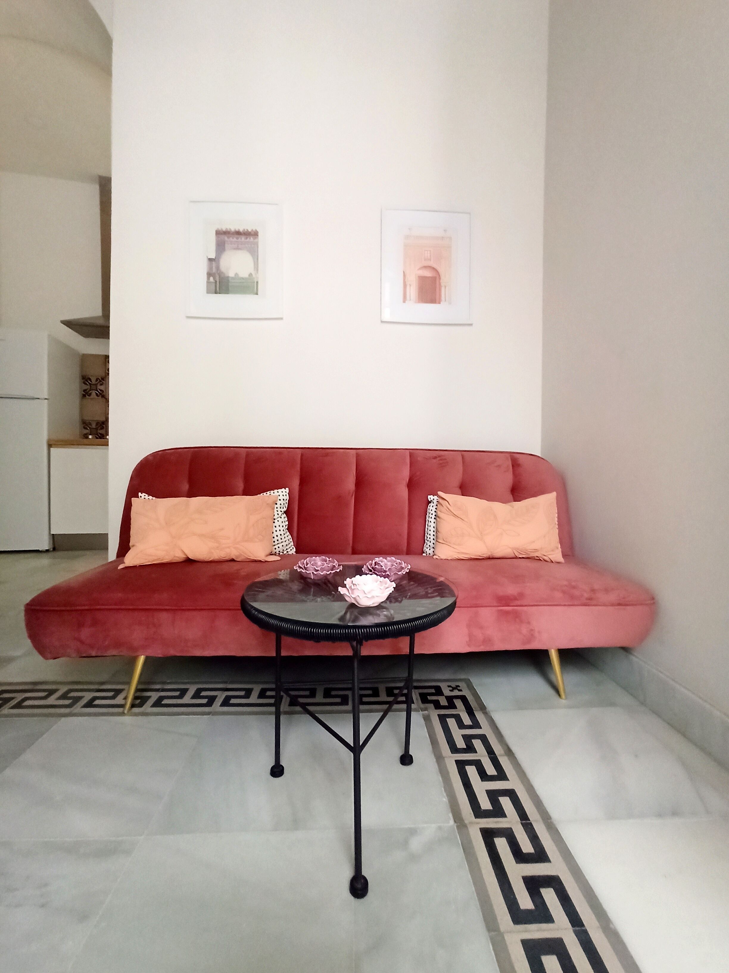 A red sofa with a glass coffee table in front, a patterned rug, and two framed pictures on the wall.