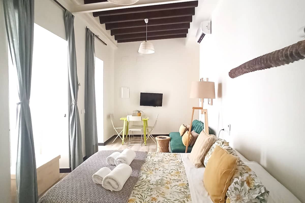 Een slaapkamer met een bed, een bureau, een stoel, een televisie en een raam met gordijnen.
