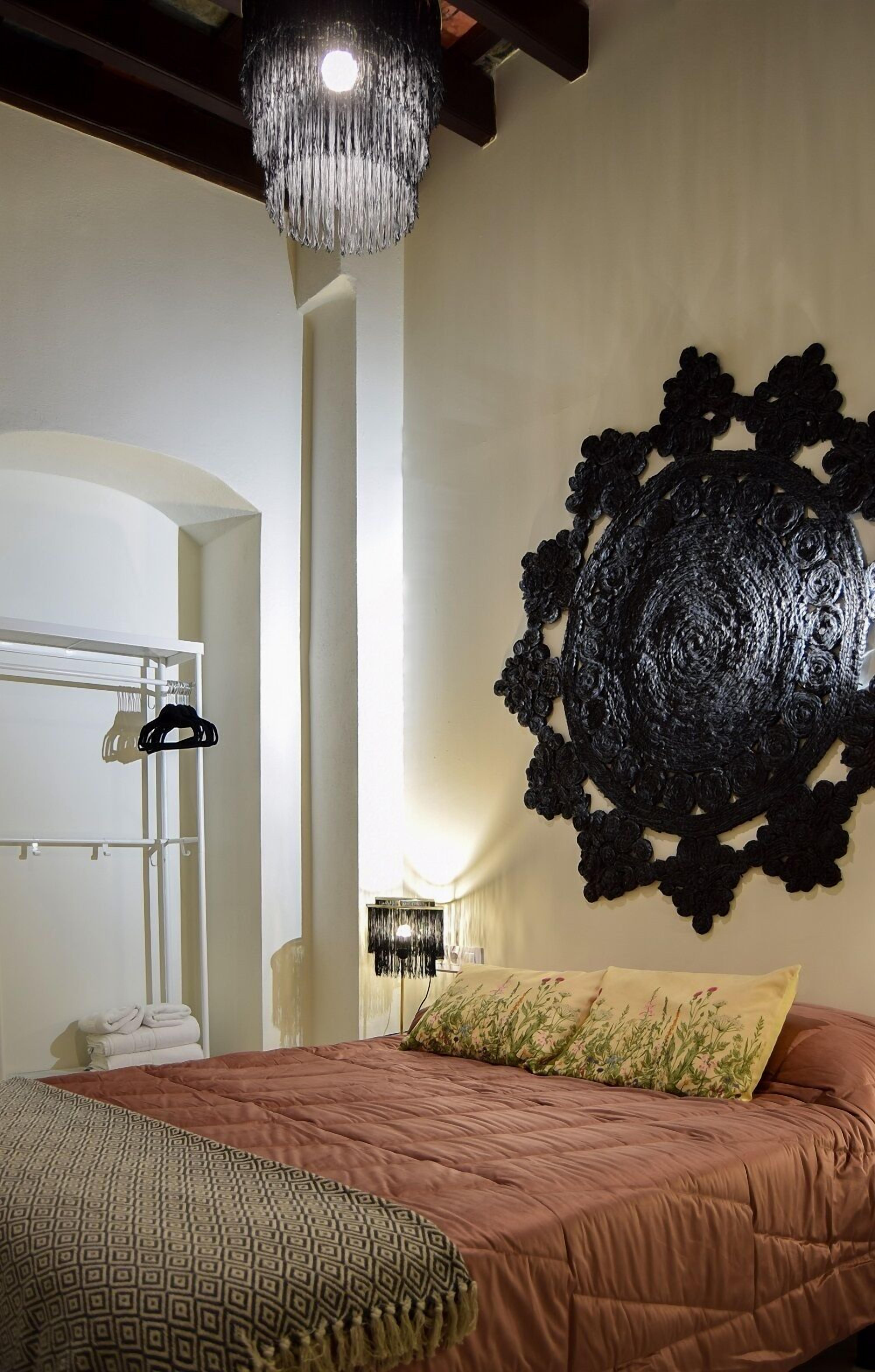 A bedroom with a large bed, a chandelier, a wall art piece, and a wardrobe.