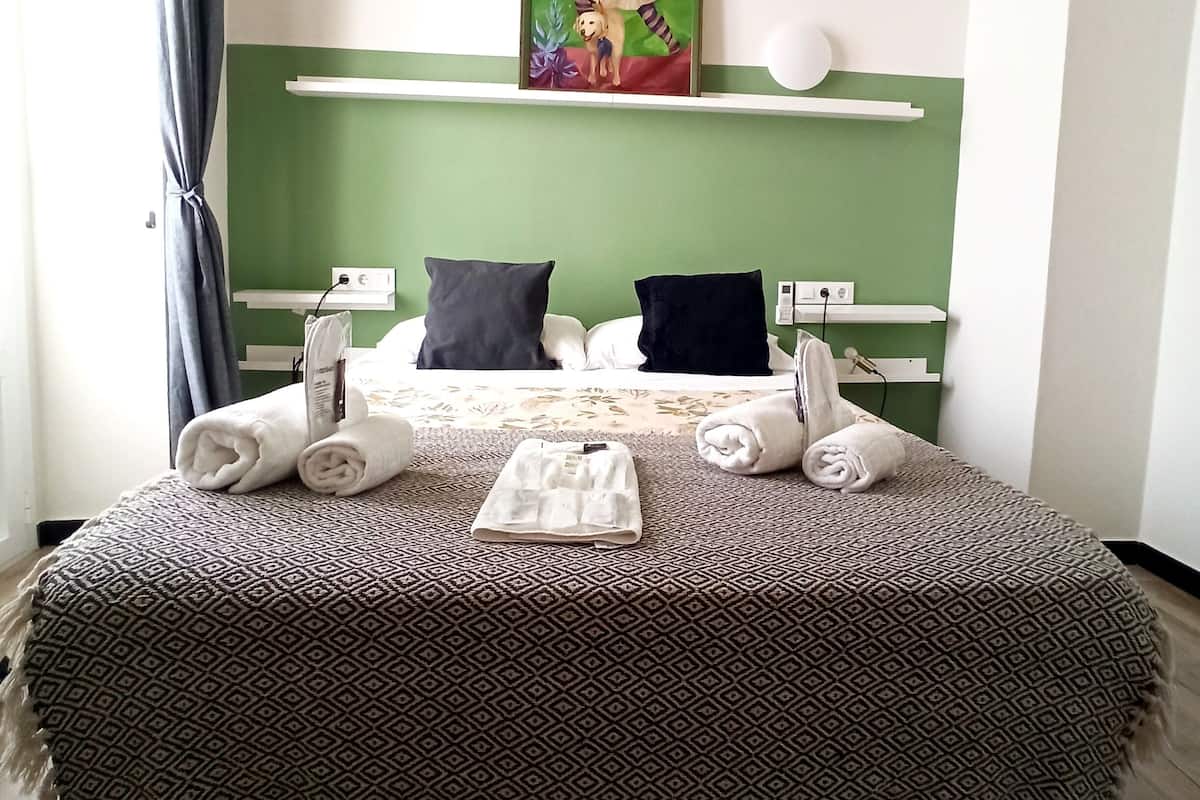 Een net opgemaakt bed met een beddekleed met patroon, twee kussens en opgerolde handdoeken aan de zijkant.