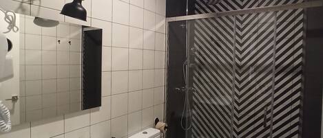 A modern bathroom with a white sink, mirror, and toilet. There is a glass shower enclosure with a black and white striped shower curtain.