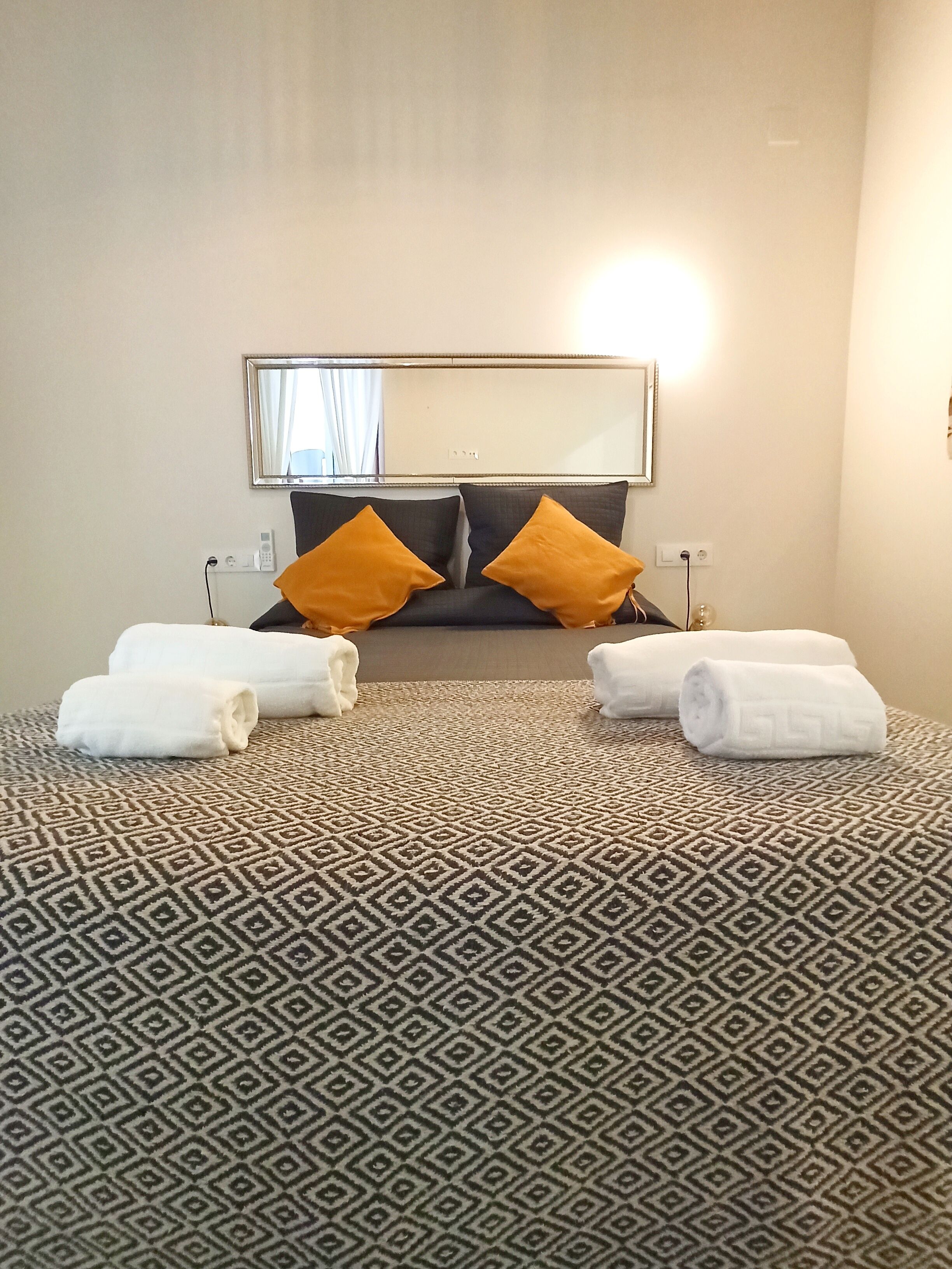 Una habitación de hotel con alfombra estampada, una cama con dos almohadas y un espejo en la pared.
