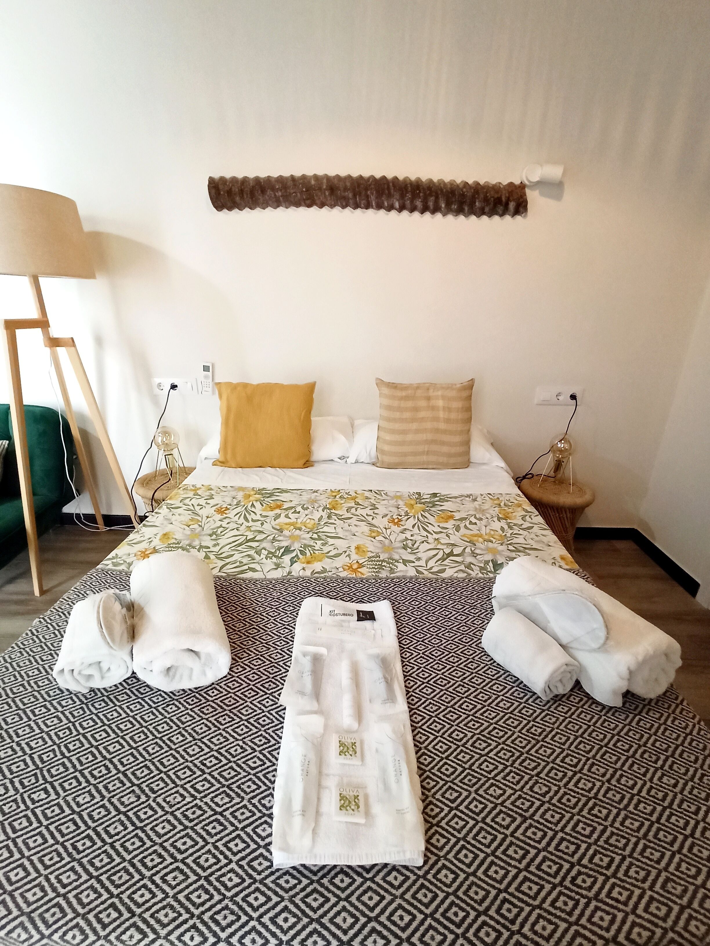 A hotel room with a bed, two pillows, a bedside table, a lamp, and a patterned rug.