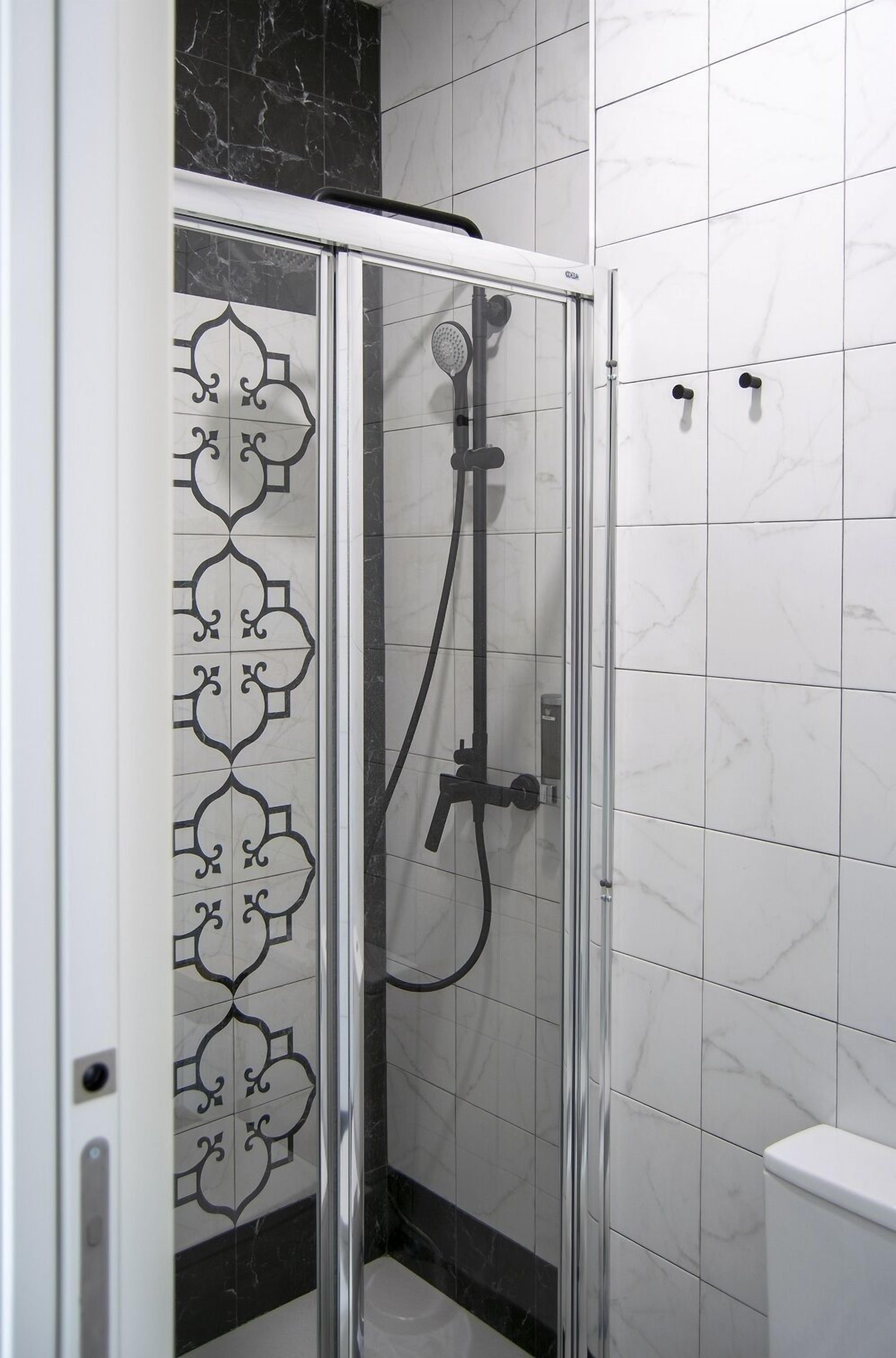 Une cabine de douche fermée par des parois en verre, dotée d’un pommeau de douche à main et d’un robinet fixé au mur.