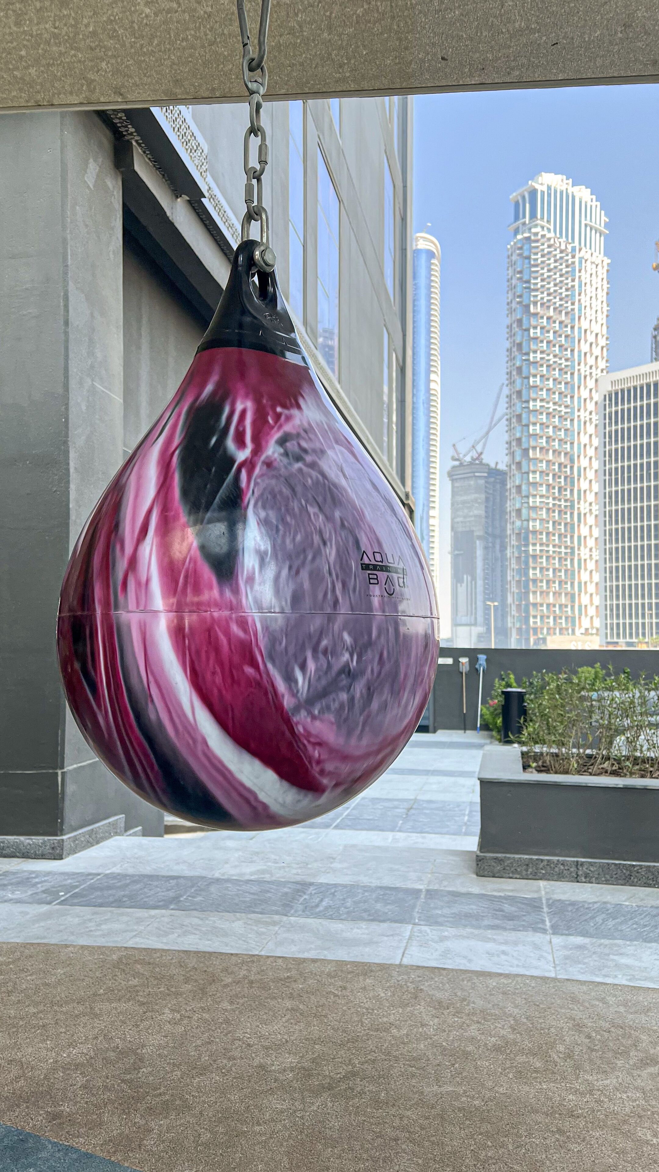 A large, spherical punching bag hanging outdoors with a cityscape in the background.