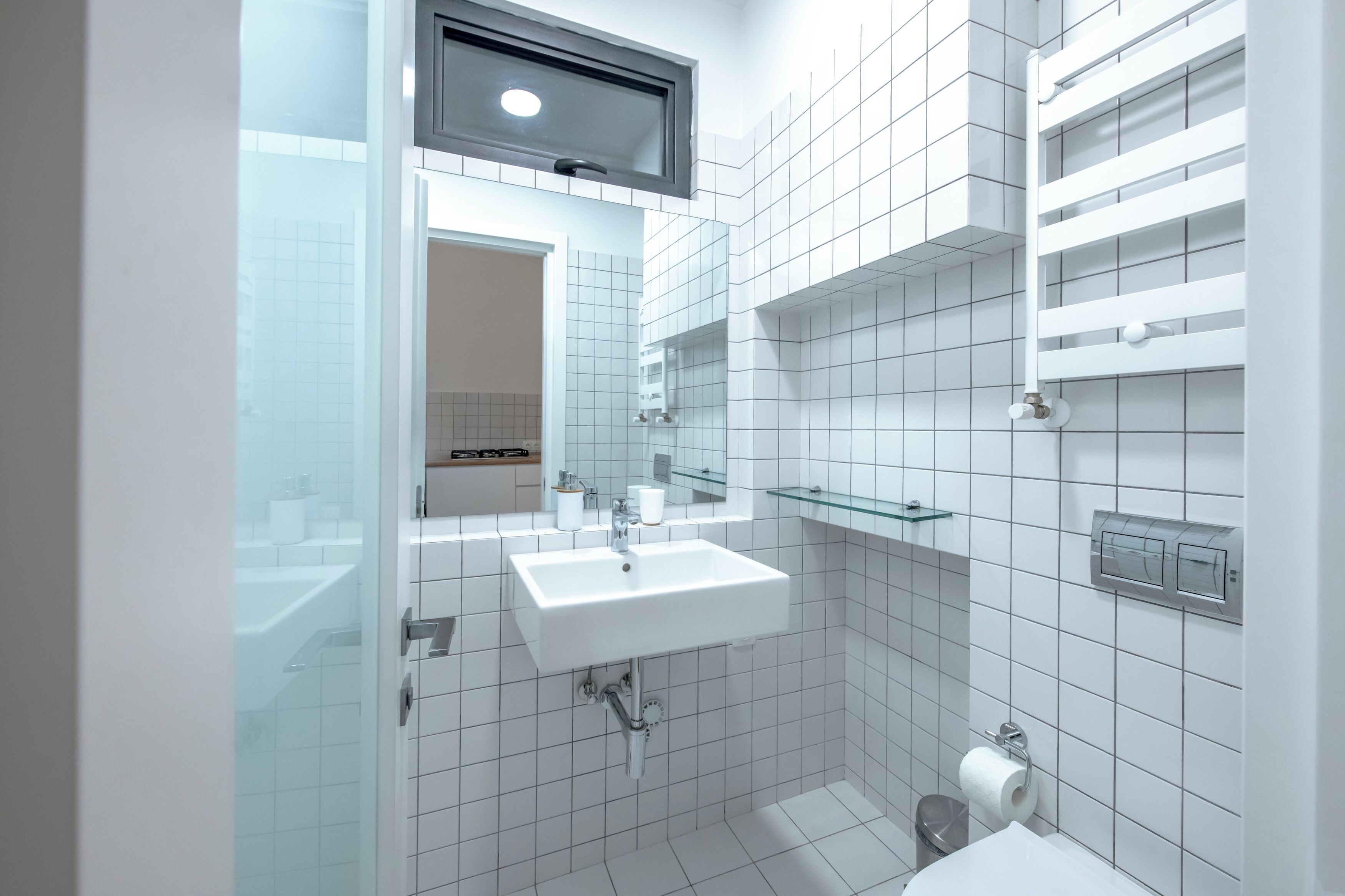 Un baño moderno con un lavabo blanco, estantes de vidrio y un espejo sobre el lavabo.