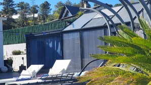 Un espace piscine aménagé avec des chaises longues, une table et une structure de serre.