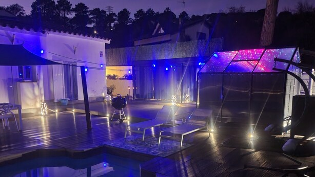 Un espace piscine aménagé avec des chaises longues, un barbecue et un éclairage d’ambiance.