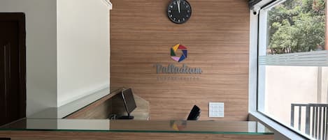 En receptionsdisk med en væg af træpaneler, et ur og et logo for 'Palladium Luxury Suites'.