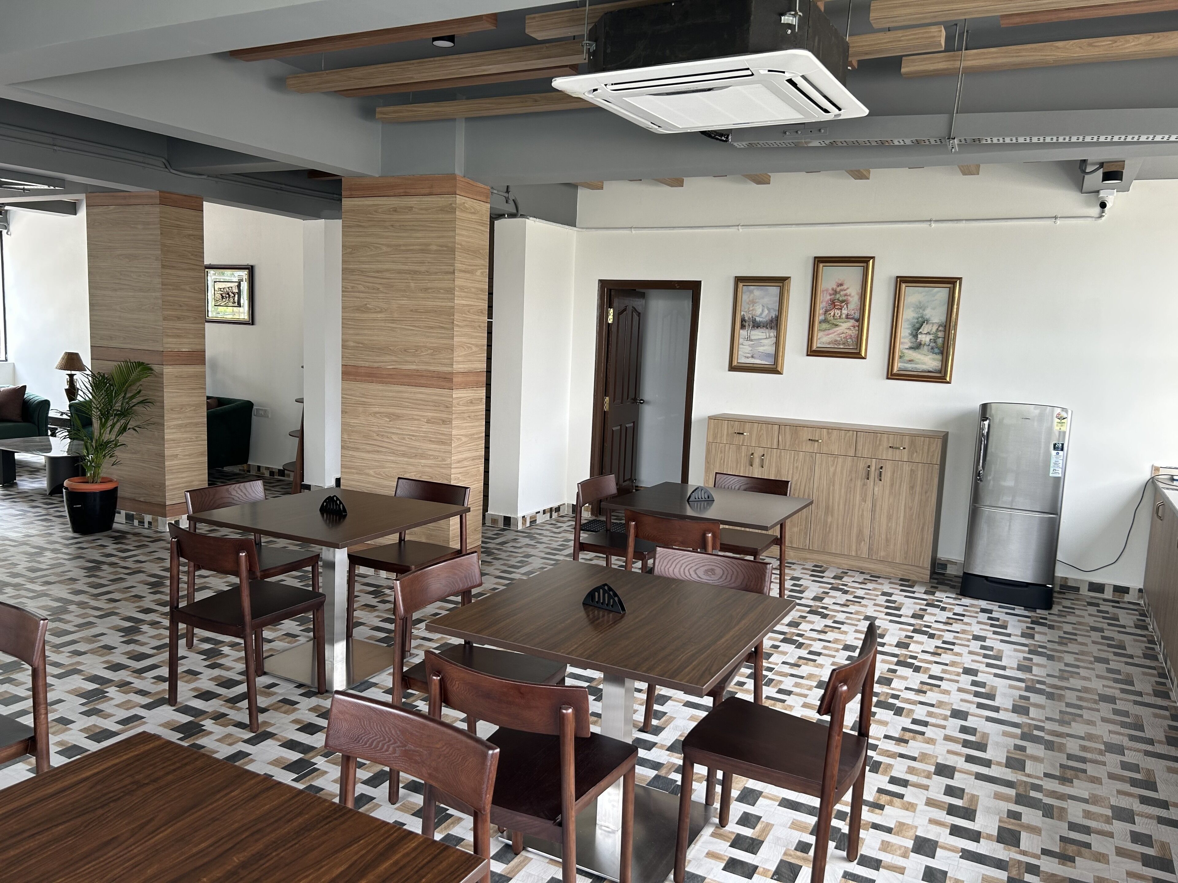 A modern dining area with wooden tables and chairs, a patterned floor, and a refrigerator.