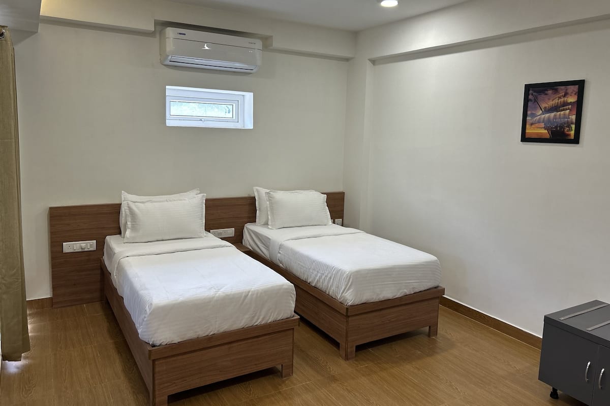 A hotel room with two wooden beds, an air conditioning unit, a ceiling fan, a window, and a small cabinet.