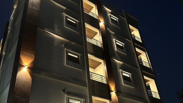 A multi-story building with illuminated windows and balconies, a visible sign with contact information, and a clear view of the building's facade. - Palladium Luxury Suites Unit II (Hyderabad)