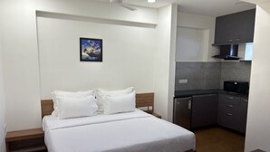 A bedroom with a bed, pillows, a nightstand, a ceiling fan, and a small kitchen area with a microwave and cabinets. - Palladium Luxury Suites Unit II (Hyderabad)