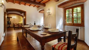 A dining area with a wooden table set for four, a chandelier, and a window with a view of greenery. - Villa Perla - Homelike Villas (Reggello)