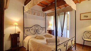 A four-poster bed with a canopy, two bedside lamps, a wooden nightstand, and a chair in a room with wooden flooring and a picture on the wall. - Villa Perla - Homelike Villas (Reggello)